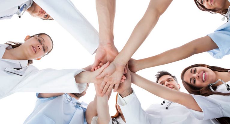 Ärzte und Krankenschwestern stehen im Kreis und halten in der Mitte die Hände aufeinander.