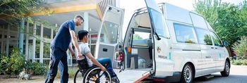 Pflegekraft fährt Patientin im Rollstuhl in einen Kleinbus