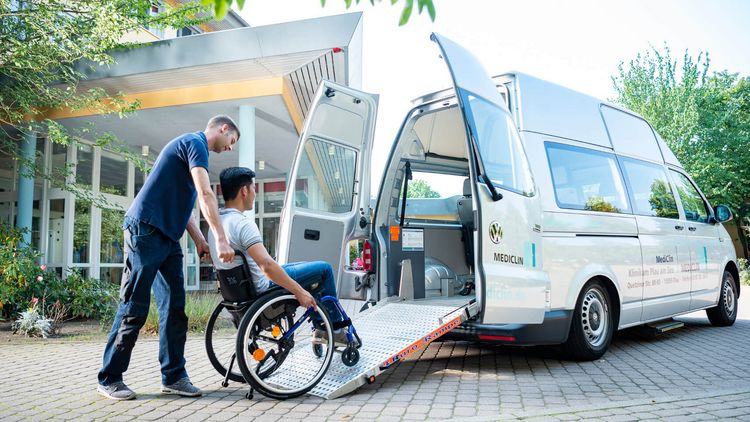 Fahrtdienst schiebt Patient im Rollstuhl in einen Kleinbus