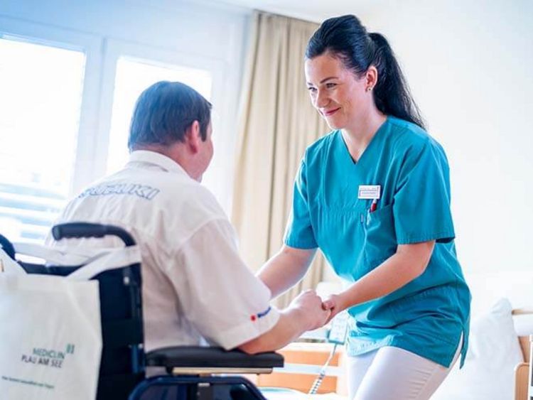 Pflegekraft hilft Patientin aus dem Rollstuhl