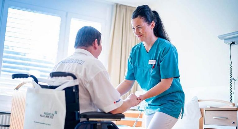 Pflegekraft hilft Patientin aus dem Rollstuhl