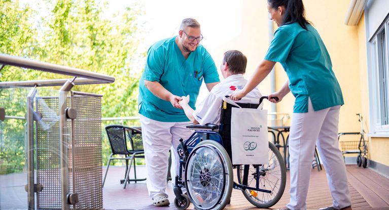 Pflegekräfte kümmern sich um Patienten im Rollstuhl